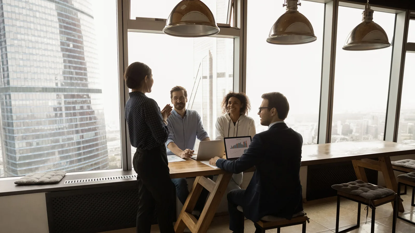 Equipe reunida em torno de uma mesa de escritório, com vista da cidade ao fundo